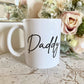white mug with daddy printed on in a script font. the mug is on a marble effect surface with a flower bouquet behind