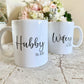 set of two white mugs. Each has a script font printed on, one says hubby the other wifey. Both mugs have est. 2020 printed beneath the script in a smaller font