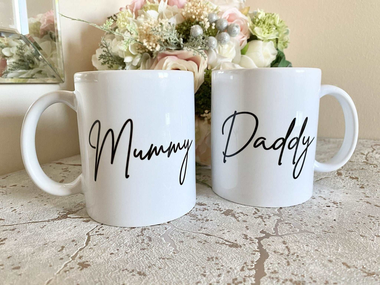 set of two white mugs. One has the text mummy printed on in a script font, the other has daddy printed on