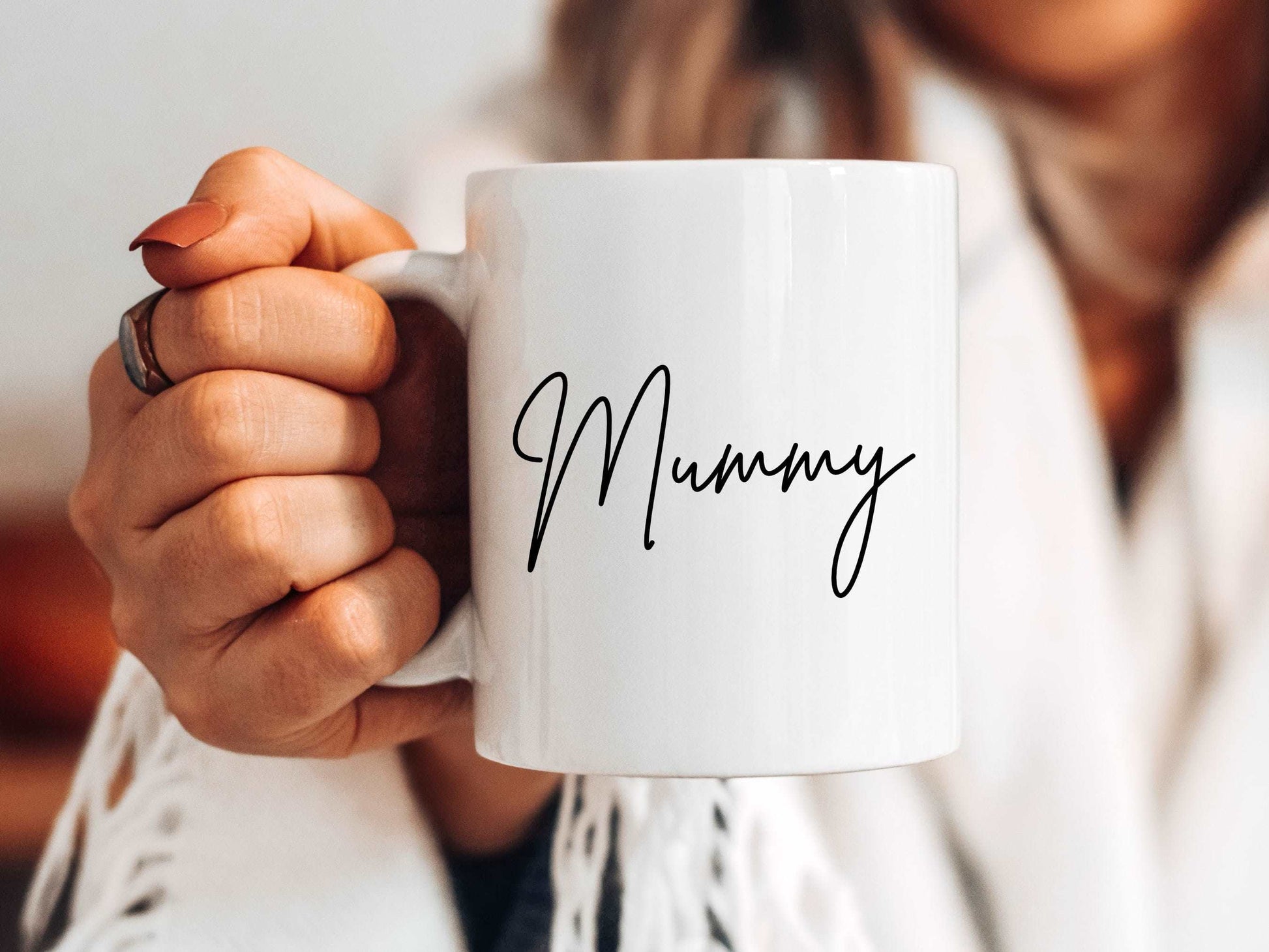 woman holding a white mug out in front of her. The mug has the text mummy printed on in a script font.