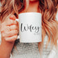 a woman holding a white mug with the text wifey printed on in a script font with est. 2022 in a slim font below